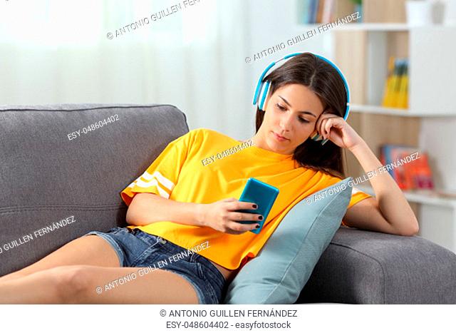 Relaxed girl in yellow listening to music sitting on a couch in the living room at home