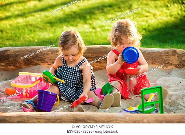 The two little baby girls two-year old playing toys in sand against green grass