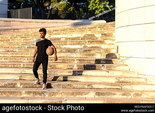 Young man with basketball moving down on steps during sunset