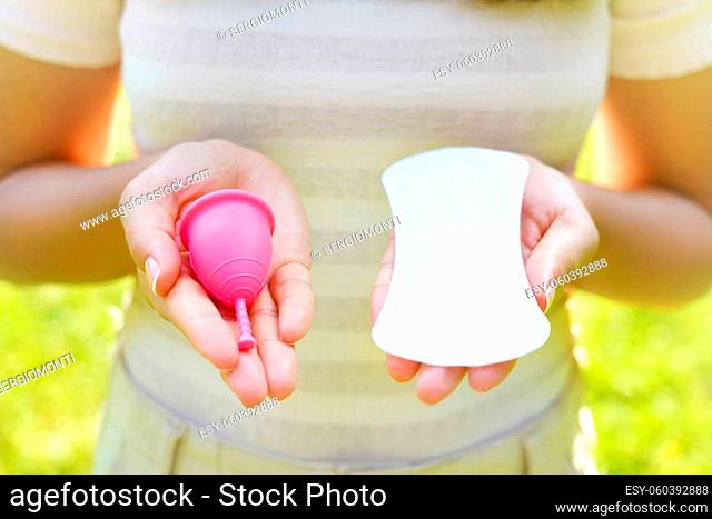 Young woman showing menstrual cup and sanitary pad in hands against green natural background. Feminine hygiene alternative product instead of tampon during her...