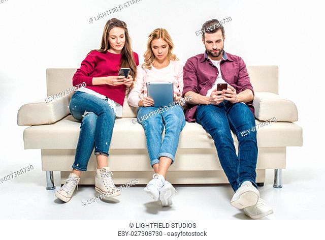 Concentrated young people sitting on couch and using digital devices
