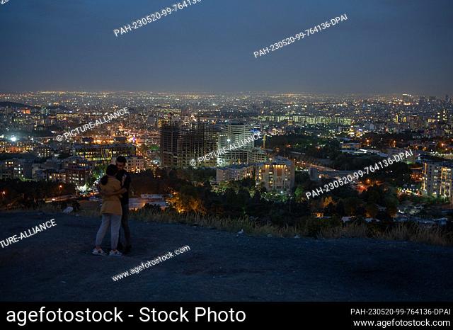 20 May 2023, Iran, Teheran: A young couple stands in front of the Tehran skyline in the east of the metropolis of millions after sunset