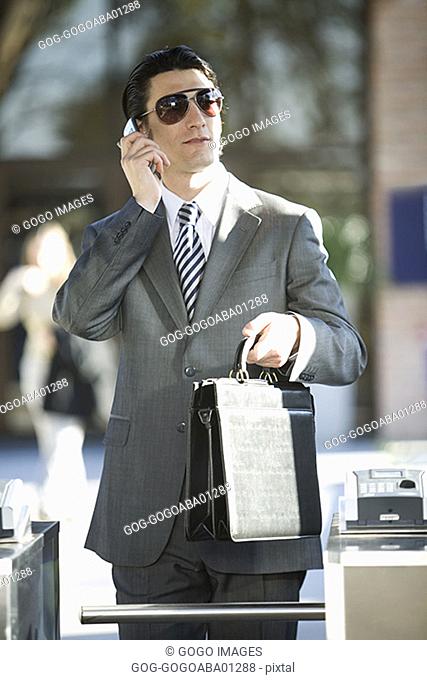 Businessman walking through turnstile while talking on cell phone