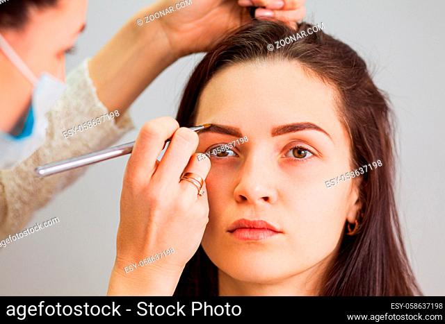 Master makeup corrects and gives shape to eyebrows in a beauty salon. Professional care for face