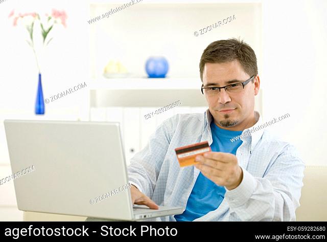 Casual man at home using laptop computer purchasing by credit card