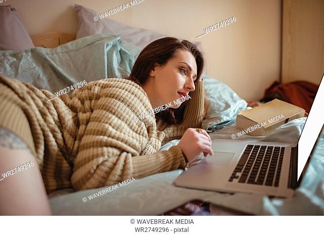 Woman lying and using laptop on bed