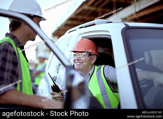 Two male construction workers chatting by car