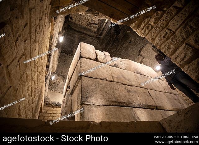 05 March 2020, Egypt, Saqqara: A custodian stands next to a sarcophagus in the Pyramid of Djoser in Saqqara ouyside Cairo