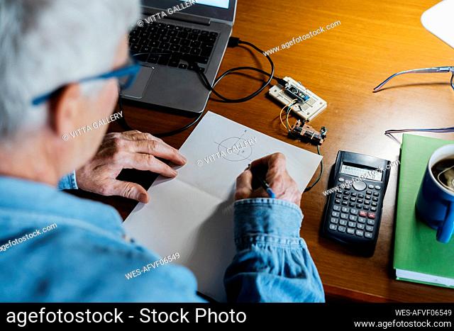 Senior man making diagram on paper while repairing laptop at home