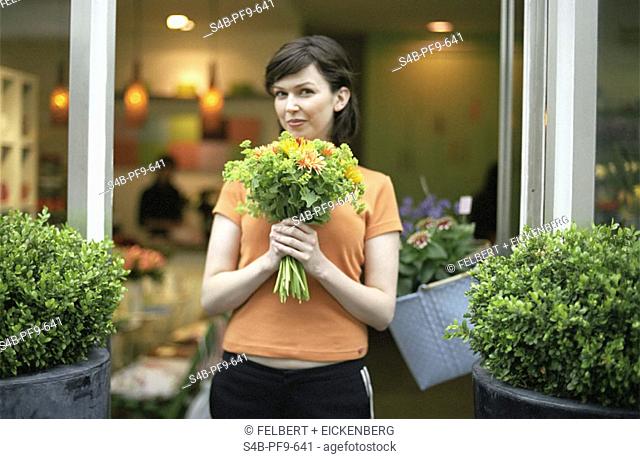 Mid adult woman with brown hair holding a bouquet in her hands between two pots of bushes, focus on foreground