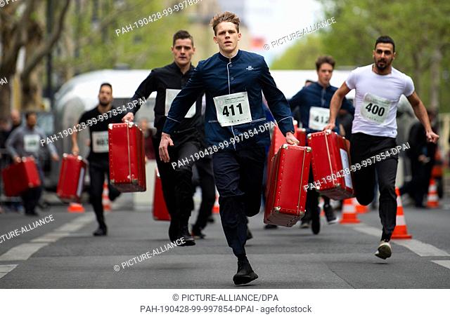 28 April 2019, Berlin: Pagen run with filled suitcases over the Kurfürstendamm at the 9th Berliner Kellnerlauf. Waiters, barkeepers