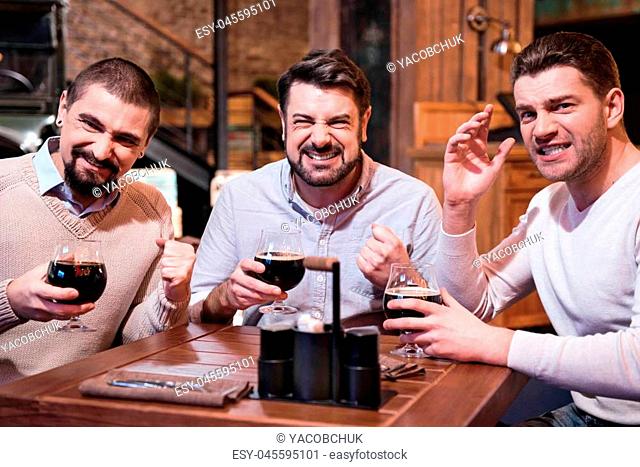 Watching TV. Positive joyful emotional men sitting at the table and supporting their football team while watching sports games in the pub