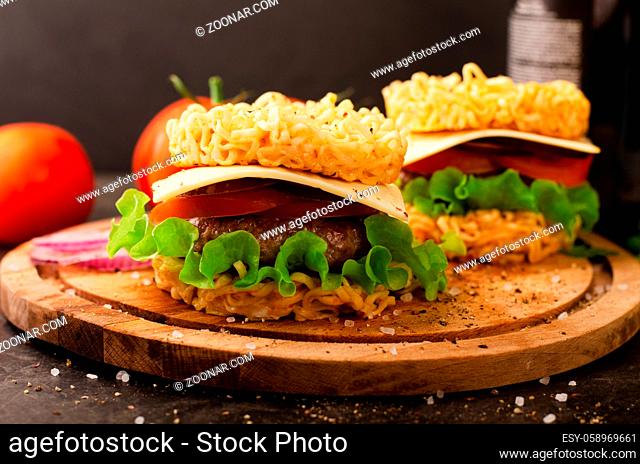 Burger with ramen, salad and tomatoes on a cutting board