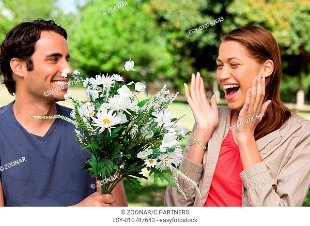 Woman laughing excitedly as she is presented with flowers by her friend