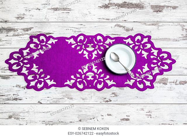 White wooden table set up with enamel plate, spoon and a decorative purple runner
