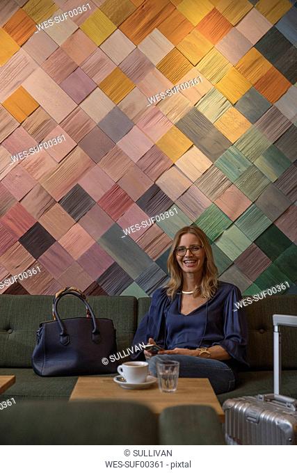 Portrait of laughing businesswoman with baggage and cell phone in a cafe