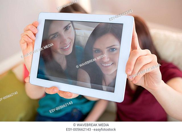 Two happy friends on the couch taking a selfie with tablet pc