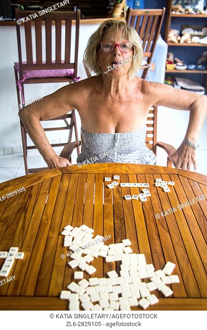 Older mature senior blond caucasian woman in her 60's , 70's playing scrabble, bananagram letters and words board game on a wood table