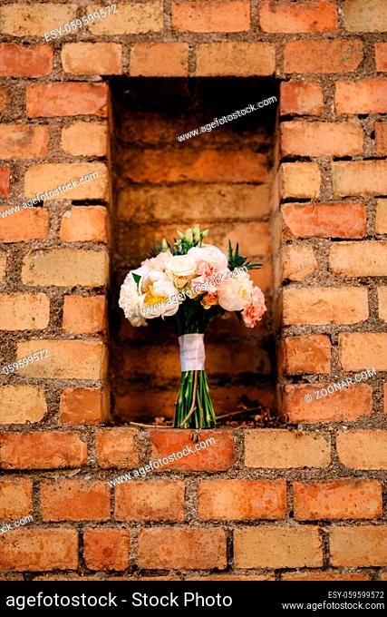 bridal bouquet of white and pink peonies, eryngium and green buds, with white ribbons down on a brick wall. High quality photo