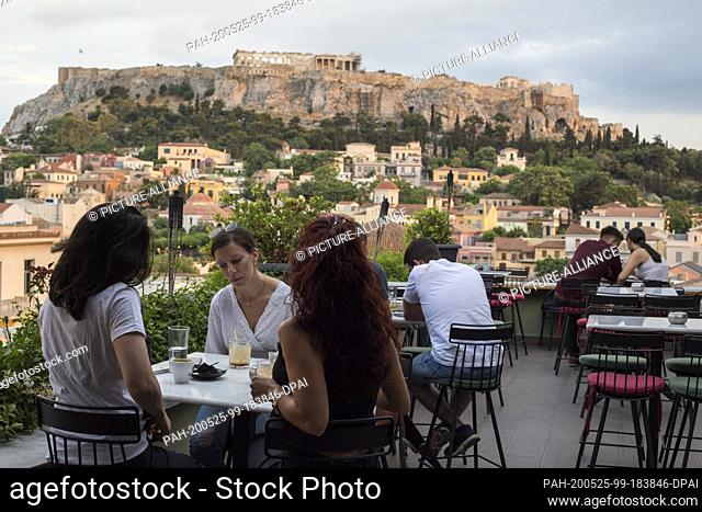 25 May 2020, Greece, Athen: Guests sit in a cafe in the Monastiraki district with the Acropolis in the background. Greece relaxes the measures imposed because...