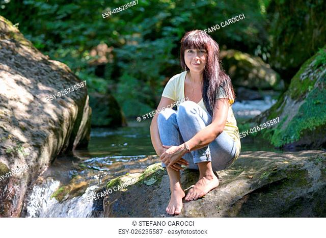 Nice girl posing on a rock in the middle of a little river