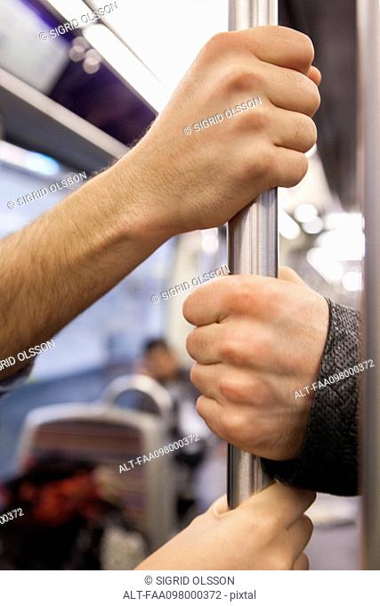 Communters on subway holding grab handle, close-up