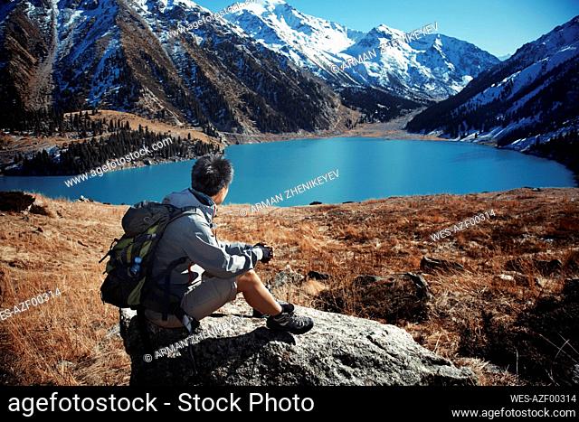 Woman with backpack looking at view while leaning on rock
