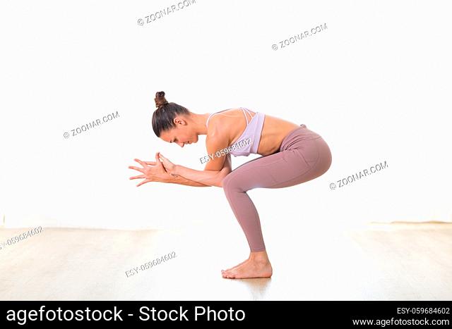 Portrait of gorgeous active sporty young woman practicing yoga in studio. Beautiful girl practice Garurasana, eagle yoga pose