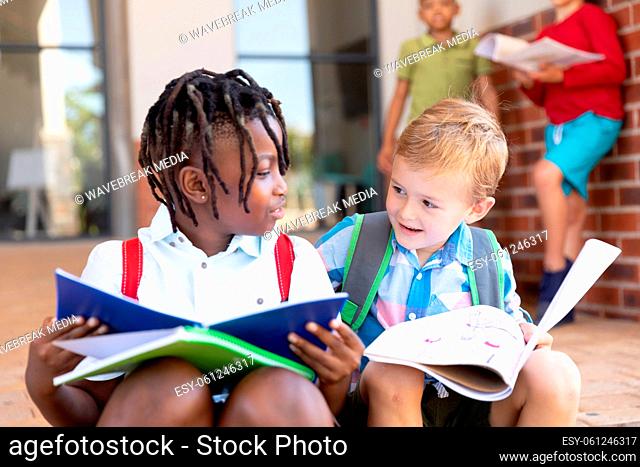 Multiracial elementary schoolboys studying while sitting on floor in school