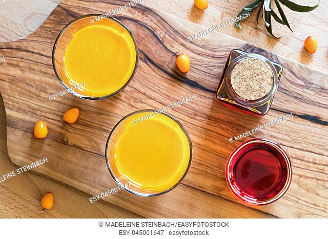 Two glasses of sea buckthorn juice, with sea buckthorn oil and berries in the background, top view