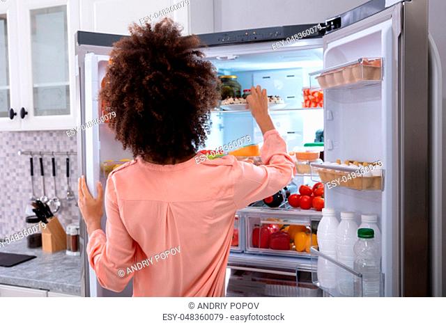 Rear View Of A Young Woman Taking Food To Eat From Refrigerator