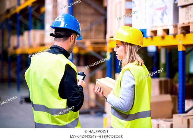 Young warehouse workers with barcode scanner working together. Man and woman discussing something