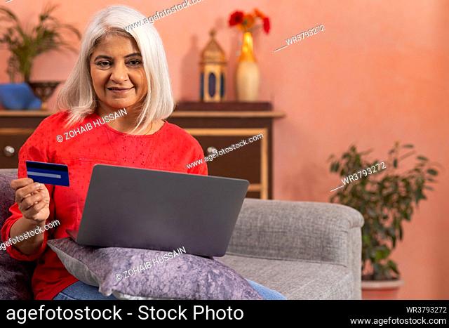 Old woman shopping online through laptop by using credit card