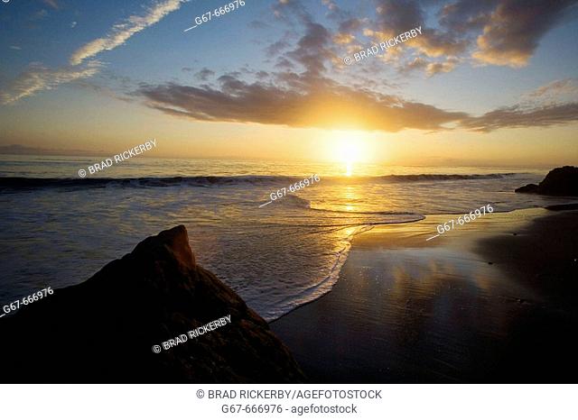 The sunset sets as clouds relect in the surf on a beach In Malibu, California, USA