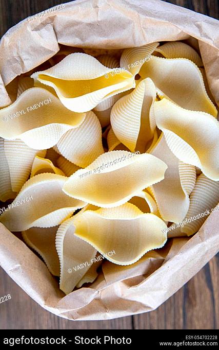 Pouch bag with pasta conchiglie flatlay, top view. Packaging on dark wooden background. Italian conchiglie or durum wheat shells