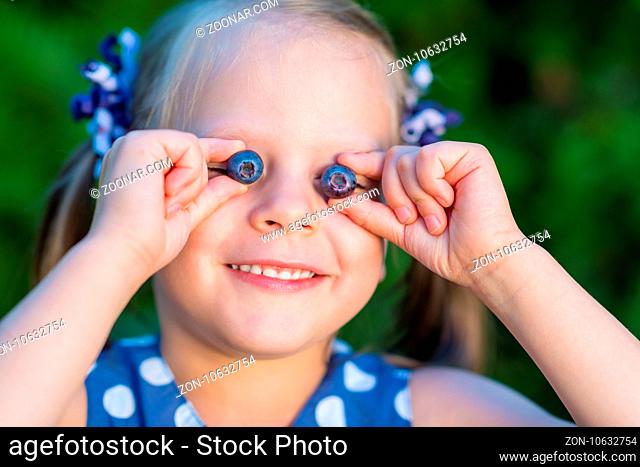 Smiling girl showing blueberries in front of her face - covering her eyes with blueberries