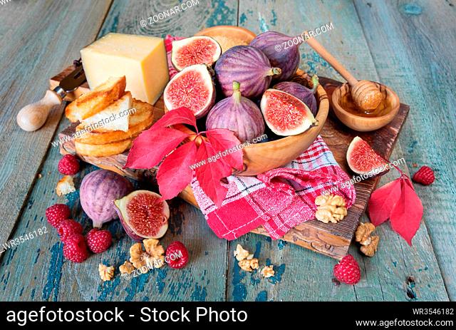 Ripe figs in a wooden bowl, red raspberry, cane sugar, honey and a checkered napkin on old cutting board as well as autumn leaves lie on the old wooden table