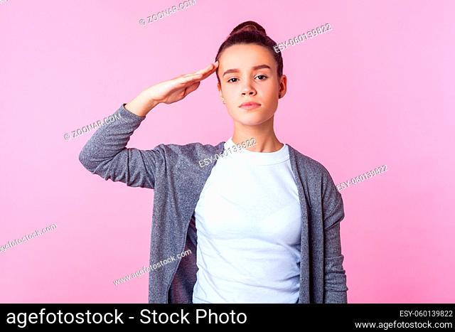 Yes sir. Portrait of obedient brunette teenage girl with bun hairstyle in casual clothes giving salute listening to order with serious responsible expression