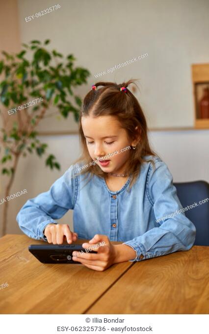 Happy kid girl playing game on mobile phone at home, child using smartphone, smartphone addiction, emotional girl