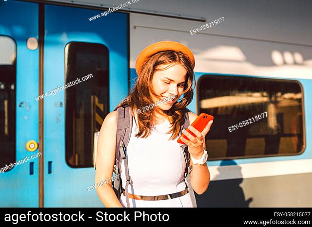 Smiling woman using smart phone on station. Young woman holding smartphone and standing at train station. Theme Transportation And Travel