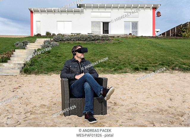 Man sitting in armchair on the beach wearing VR glasses