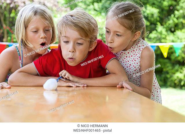 Children blowing cotton ball on garden table
