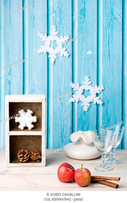 Red apples, cinnamon sticks, wine glasses, pine cone, paper snowflakes on blue wall