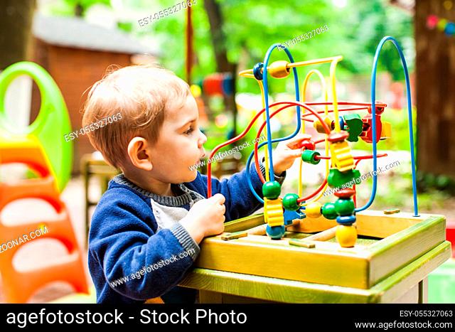Little kid boy plays with a multicolored logical labyrinth outdoor
