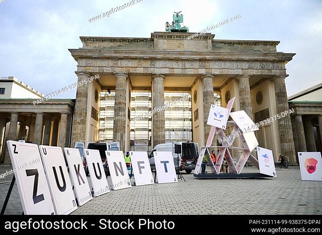 14 November 2023, Berlin: ""Future"" is written on oversized playing cards in front of the Brandenburg Gate, while a collapsed house of cards with the words...