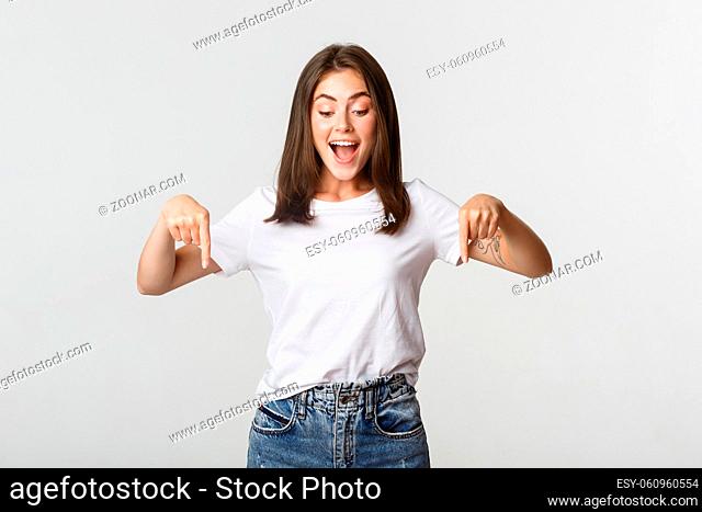 Excited happy brunette girl, looking and pointing down with amused smile