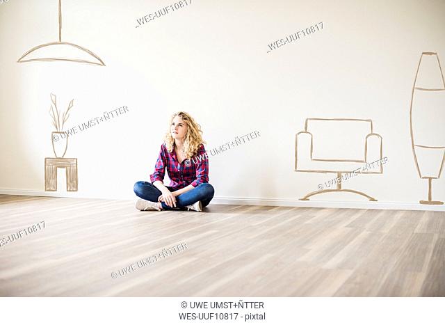 Young woman in new home sitting on floor thinking about interior design