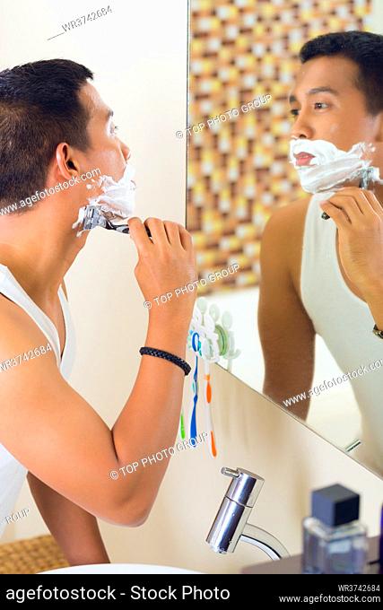 Asian man shaving in front of bathroom mirror