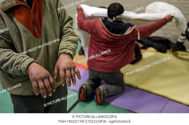 A homeless man showing his frozen hands while another man prepares his bed for the night in a gym in Hamburg, Germany, 27 February 2018