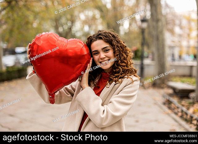 Happy woman with red heart shaped balloon at footpath
